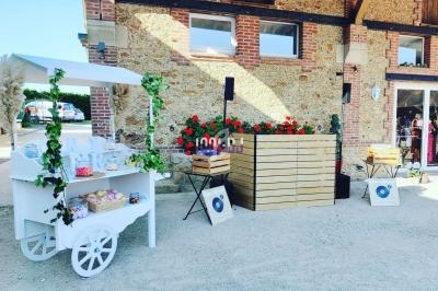 Chariot décoratif blanc avec friandises, devant un bâtiment en pierre et des caisses en bois, dans une cour extérieure.