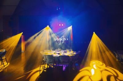 Salle sombre illuminée par des projecteurs colorés, avec une table dressée au centre entourée de chaises.