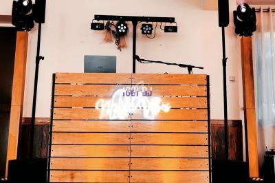 Pupitre de DJ en bois avec enseigne lumineuse, éclairages et enceintes installés dans une salle intérieure.