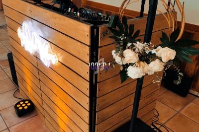 Console de DJ en bois avec éclairage LED, ornée de fleurs blanches, installée sur un sol carrelé.