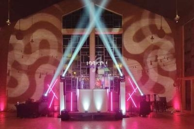 Installation lumineuse avec projecteurs colorés et jeux de lumière dans une salle avec un DJ au centre.