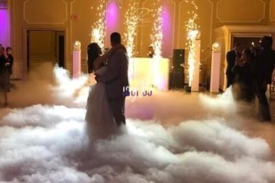 Un couple danse sur une piste enveloppée de fumée, sous un lustre et des étincelles lumineuses.