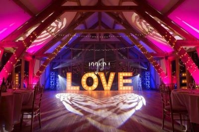 Salle de réception en bois illuminée par des guirlandes et des lettres lumineuses formant le mot ’LOVE’.