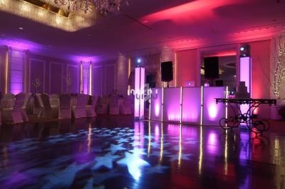 Salle de réception vide avec éclairage coloré violet et rose, chaises alignées et piste de danse brillante.