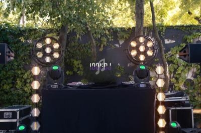 Console de DJ en extérieur, entourée de projecteurs lumineux et de végétation en arrière-plan.