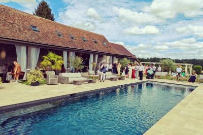 Groupe de personnes rassemblées près d'une piscine dans un jardin, devant un bâtiment en pierre avec toit en tuiles.
