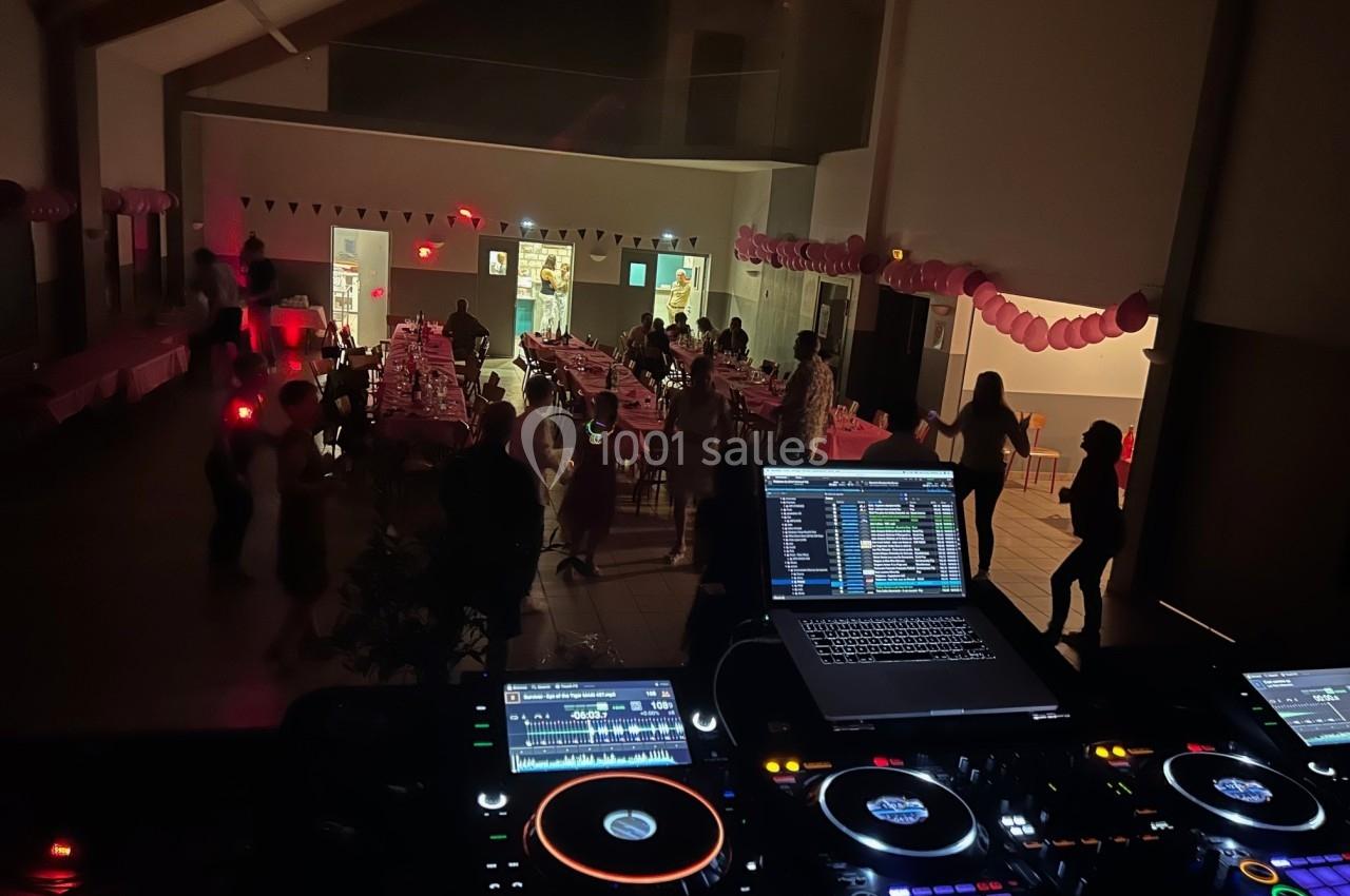 Salle de fête décorée avec des guirlandes, vue depuis une table de mixage avec des invités dansant et discutant.