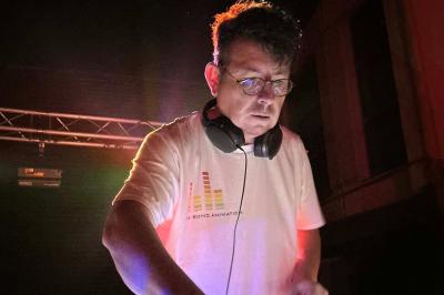 Un DJ mixant de la musique sur une table de mixage éclairée par des lumières colorées dans une ambiance sombre.