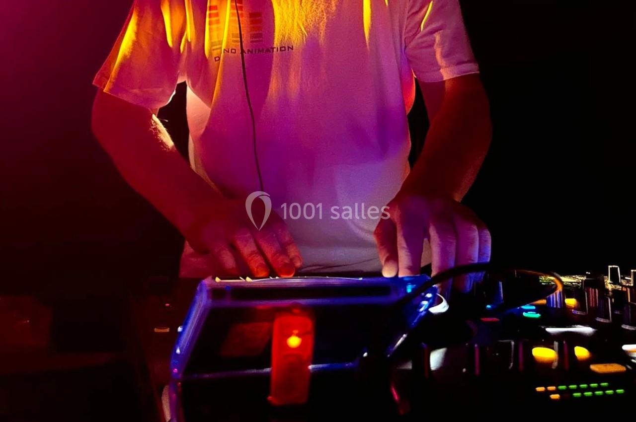 Un DJ mixant de la musique sur une table de mixage éclairée par des lumières colorées dans un environnement sombre.