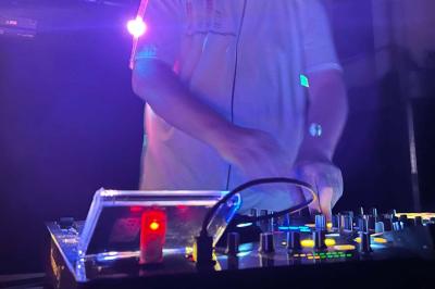 Un DJ mixant de la musique sur une table de mixage éclairée par des lumières colorées dans une ambiance sombre.