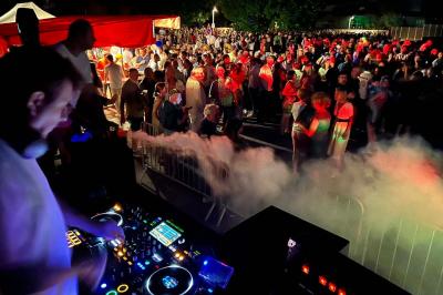 Un DJ mixe sur une table de mixage éclairée, dans une ambiance sombre avec des lumières colorées en arrière-plan.