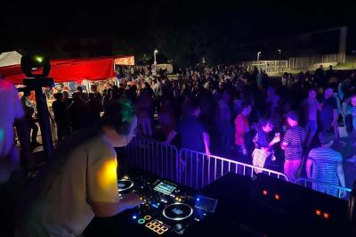 Un DJ mixe sur une table de mixage éclairée, dans une ambiance sombre avec des lumières colorées en arrière-plan.