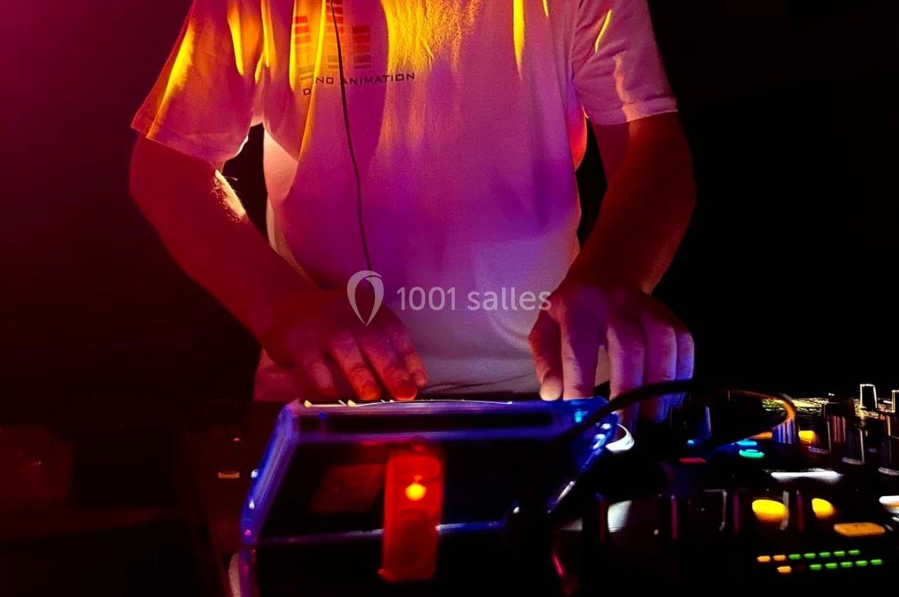 Un DJ mixant de la musique sur une table de mixage éclairée par des lumières colorées dans un environnement sombre.
