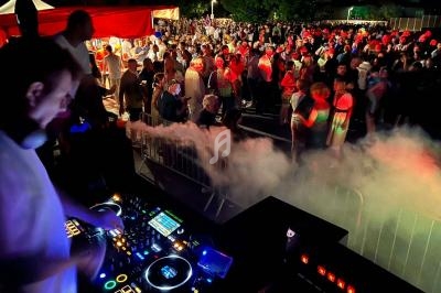 Un DJ mixe sur une scène en plein air devant une foule dense lors d'un événement nocturne festif.