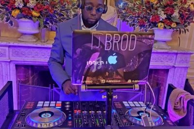 Un DJ mixant de la musique sur une table de mixage dans une salle élégante décorée de fleurs et éclairée en violet.