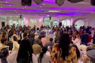 Salle de réception bondée avec des invités debout et assis, éclairage violet et décorations festives.