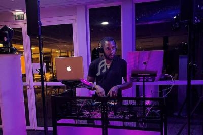 Un DJ mixe de la musique sur une table équipée d'ordinateurs et de matériel audio dans une salle éclairée en violet.