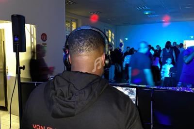 Un DJ mixant de la musique lors d'une soirée dans une salle éclairée par des lumières colorées.