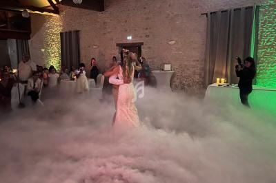 Un couple danse au milieu d'une piste enveloppée de fumée, sous le regard des invités dans une salle en pierre.