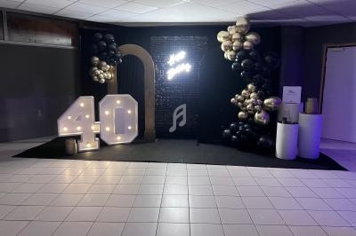 Décoration de fête avec ballons noirs et dorés, chiffre lumineux ’40’ et panneau lumineux sur fond sombre.