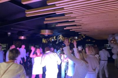 Des personnes dansent sous un éclairage coloré lors d'une fête, avec des ballons formant ’Happy Birthday’ en arrière-plan.