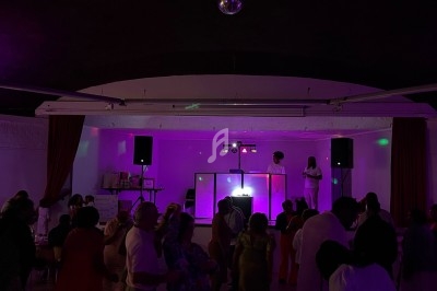 Salle sombre avec des lumières violettes, une scène avec deux personnes et des participants dansant au premier plan.