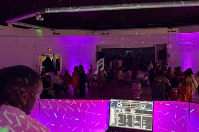 Un DJ anime une soirée dans une salle éclairée par des lumières violettes, avec des invités assis et debout.
