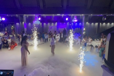 Salle de réception avec invités, éclairage coloré, fumée au sol et jets d'étincelles lors d'un événement festif.