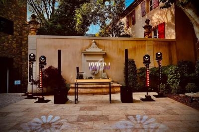 Installation de matériel audio et éclairage devant une fontaine, dans une cour extérieure bordée d'arbres et de bâtiments.