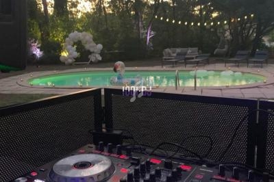 Table de mixage éclairée au premier plan, avec une piscine et un jardin décoré en arrière-plan au crépuscule.