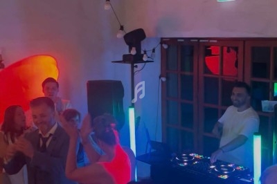 Des invités dansent et célèbrent autour d'un DJ dans une salle éclairée par des lumières colorées.