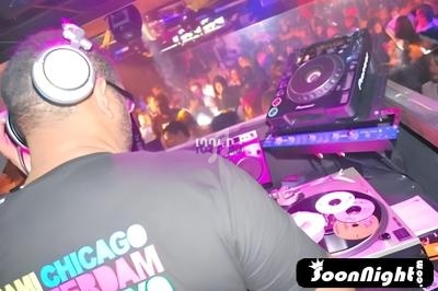 Un DJ mixe sur des platines dans une boîte de nuit animée avec une foule dansante en arrière-plan.