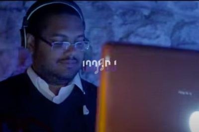 Homme portant un casque audio, concentré devant un ordinateur portable éclairé dans une ambiance tamisée.