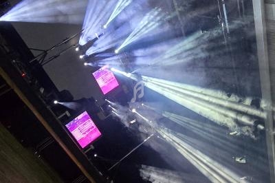 Projecteurs diffusant des faisceaux lumineux à travers de la fumée dans une salle sombre avec des écrans allumés.