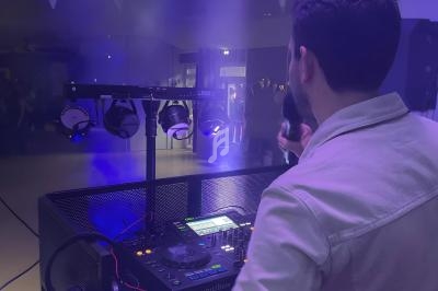Un DJ de dos, tenant un micro, anime une soirée dans une ambiance lumineuse avec des projecteurs et de la fumée.