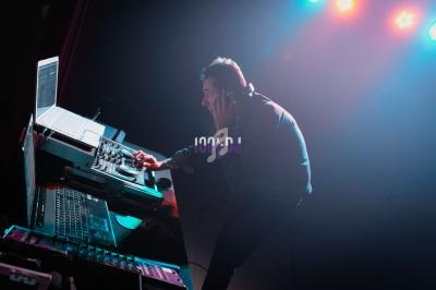 Un DJ mixe de la musique sur une table de mixage éclairée par des lumières colorées dans un environnement sombre.