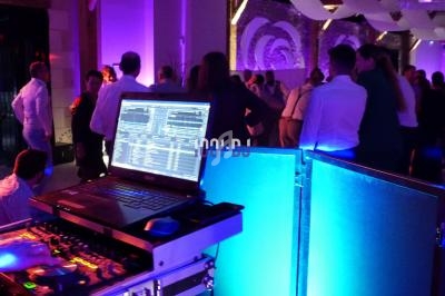 Ordinateur portable et table de mixage dans une ambiance festive avec des personnes dansant sous des lumières colorées.