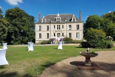 Manoir entouré de verdure avec des tables hautes blanches disposées sur une pelouse.