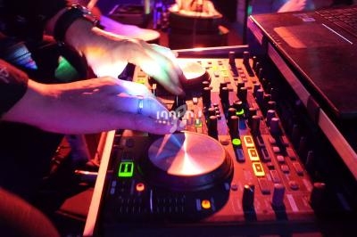 Mains manipulant une table de mixage avec des lumières colorées en arrière-plan.