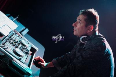 Un DJ portant un casque écoute attentivement près d'une table de mixage éclairée par une lumière tamisée.