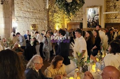 Personnes rassemblées dans une salle en pierre décorée pour un événement, avec tables dressées et ambiance chaleureuse.