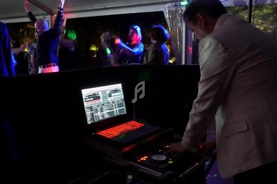 Un DJ en costume mixe de la musique sur un ordinateur portable lors d'une soirée dansante sous une tente éclairée.