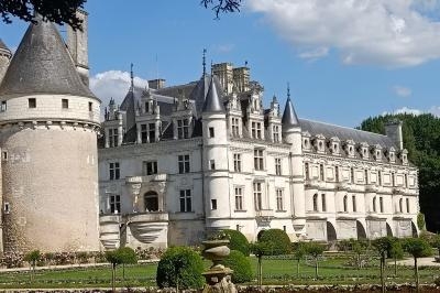 Façade d'un château Renaissance entouré de jardins fleuris sous un ciel partiellement nuageux.