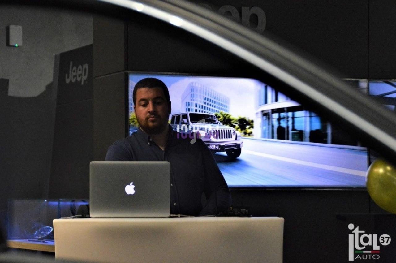Homme debout devant un ordinateur portable, avec une image de véhicule Jeep affichée en arrière-plan.