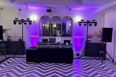 Configuration d'un espace DJ avec platines, enceintes et éclairage violet dans une salle au sol en chevrons.