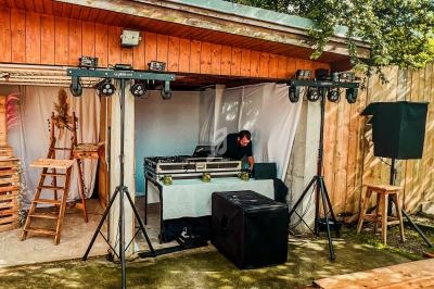 Un DJ prépare son matériel sous un abri en bois, entouré de projecteurs et d'équipements audio en extérieur.
