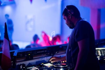 Un DJ mixe de la musique sur une table de mixage dans une salle éclairée par des lumières colorées.