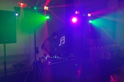 Un DJ mixe de la musique sur une table de mixage, entouré de lumières colorées dans une ambiance festive.
