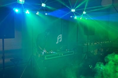 Un DJ mixant sur une table de mixage entourée de lumières colorées et de fumée dans une ambiance festive.