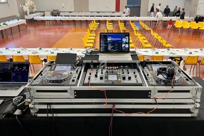 Table de mixage DJ avec ordinateurs et casques en premier plan, dans une salle de réception avec tables dressées.